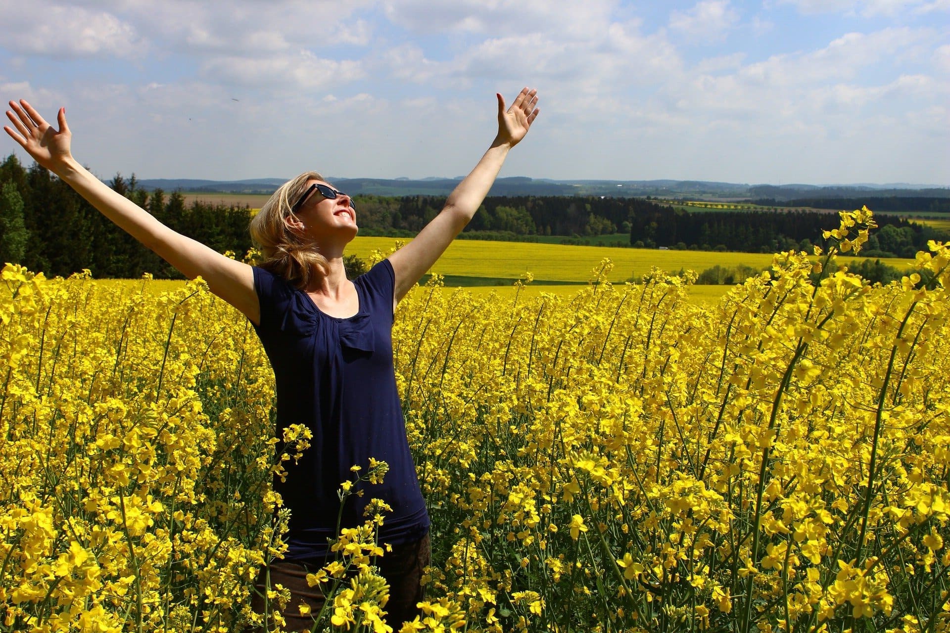 Femme souriante bras ouverts dans un champ de fleurs jaunes